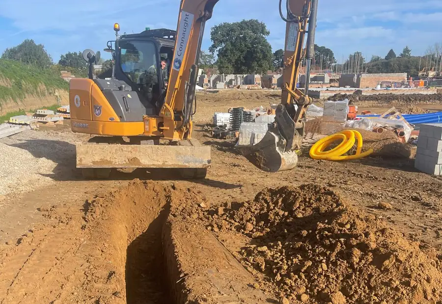 A wheeled excavator beside an open, battered excavation on a housing development