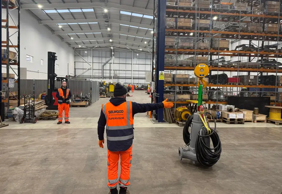 Lifting equipment and accessories laid out on the floor of a warehouse, with people in hi-vis alongside